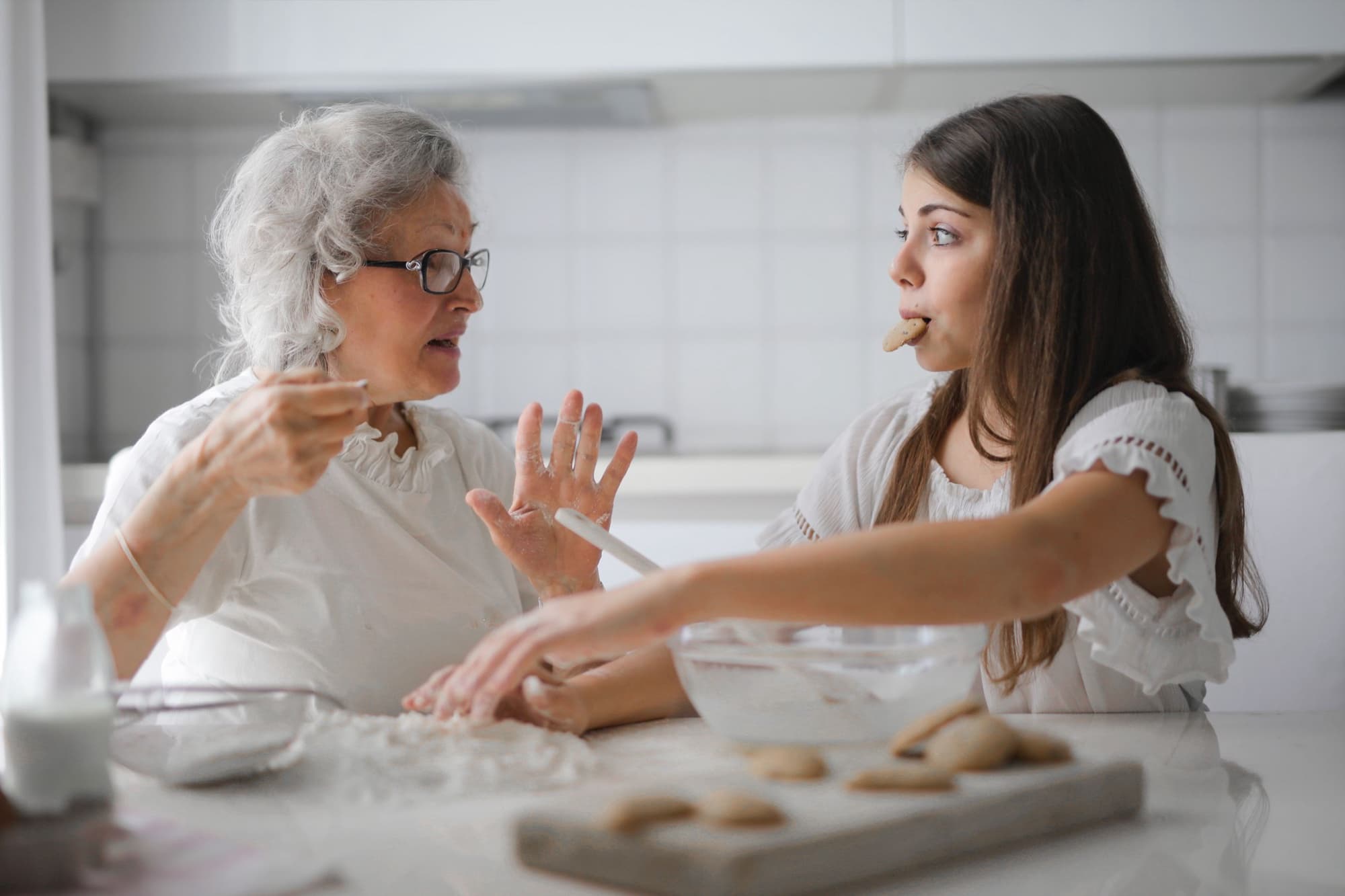 An older woman and a young girl make biscuits together at a kitchen counter.